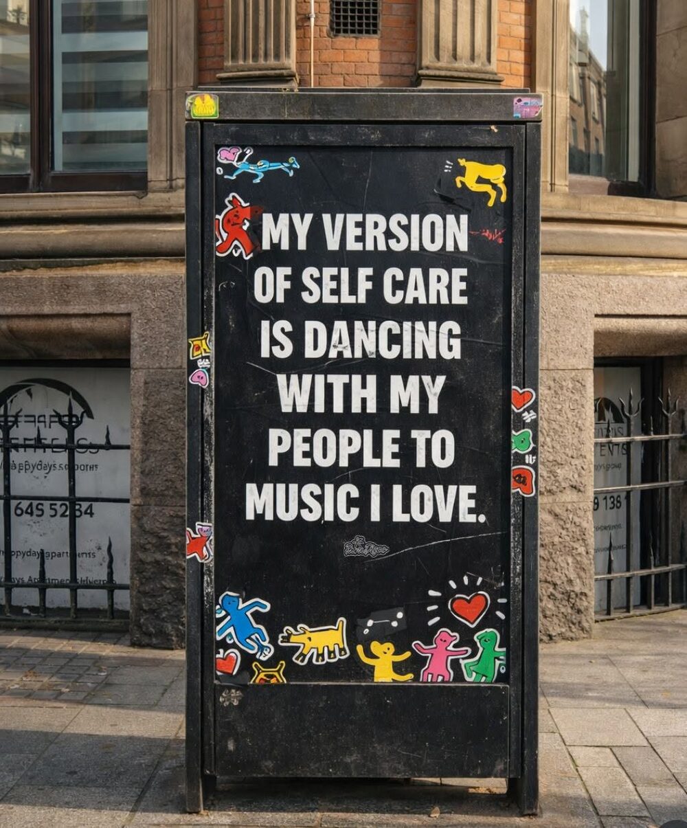 A chalkboard sign on the street reading: My version of self care is dancing with my people to music I love