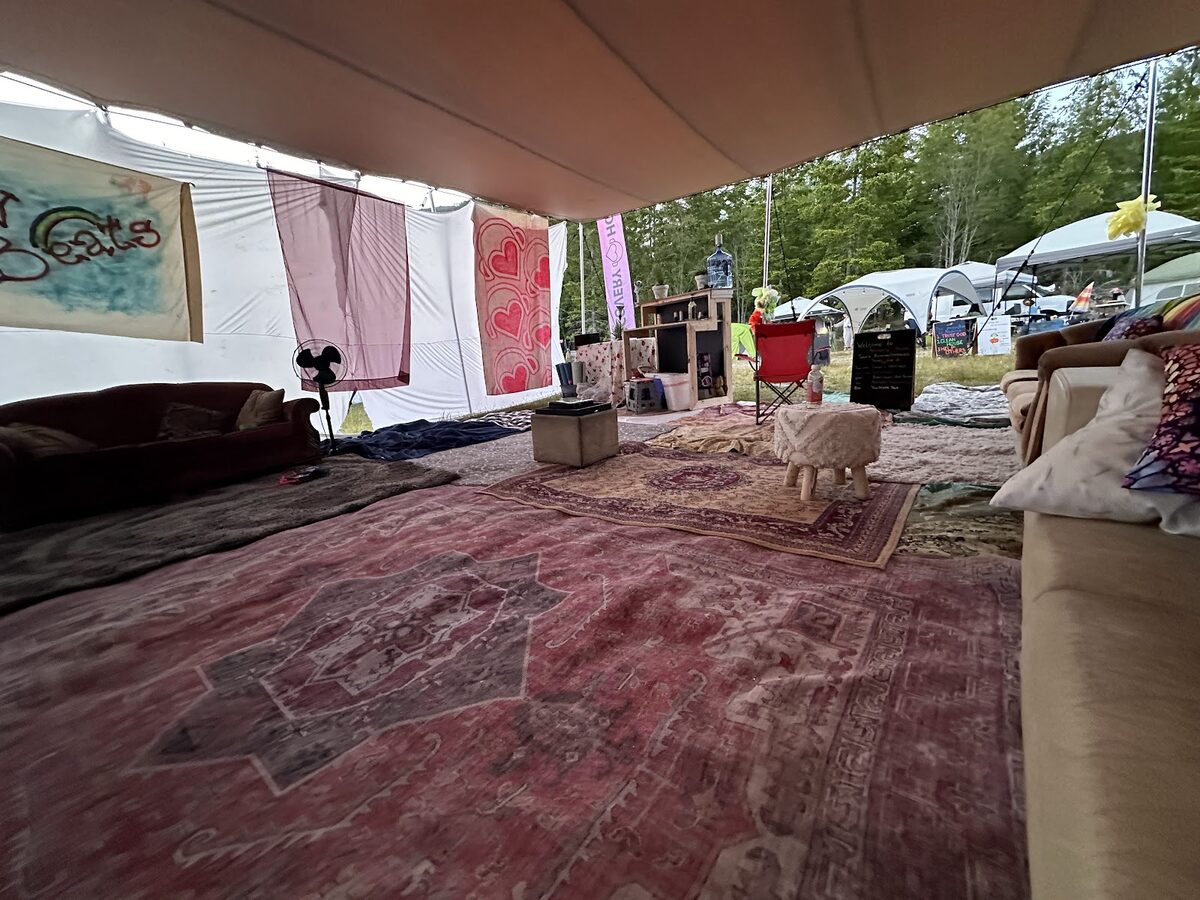 Inside the Recovery House stretch tent at Otherworld: layered Persian rugs, couches, and a hand-painted Clean Beats banner on the wall