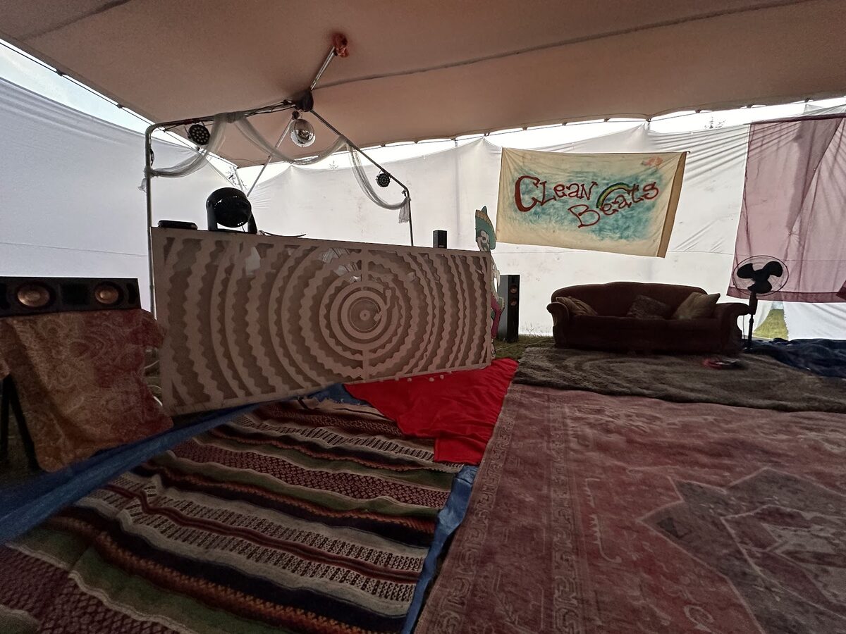 The DJ booth inside the Recovery House tent, under a hand-painted Clean Beats banner, with rugs and a couch in front